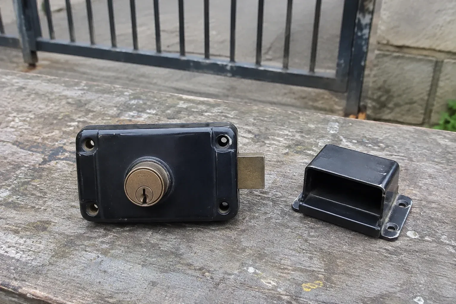 Detached rim gate lock and separate box keeper on an outdoor workbench. — Gate & Building Entry Locks, Oakville