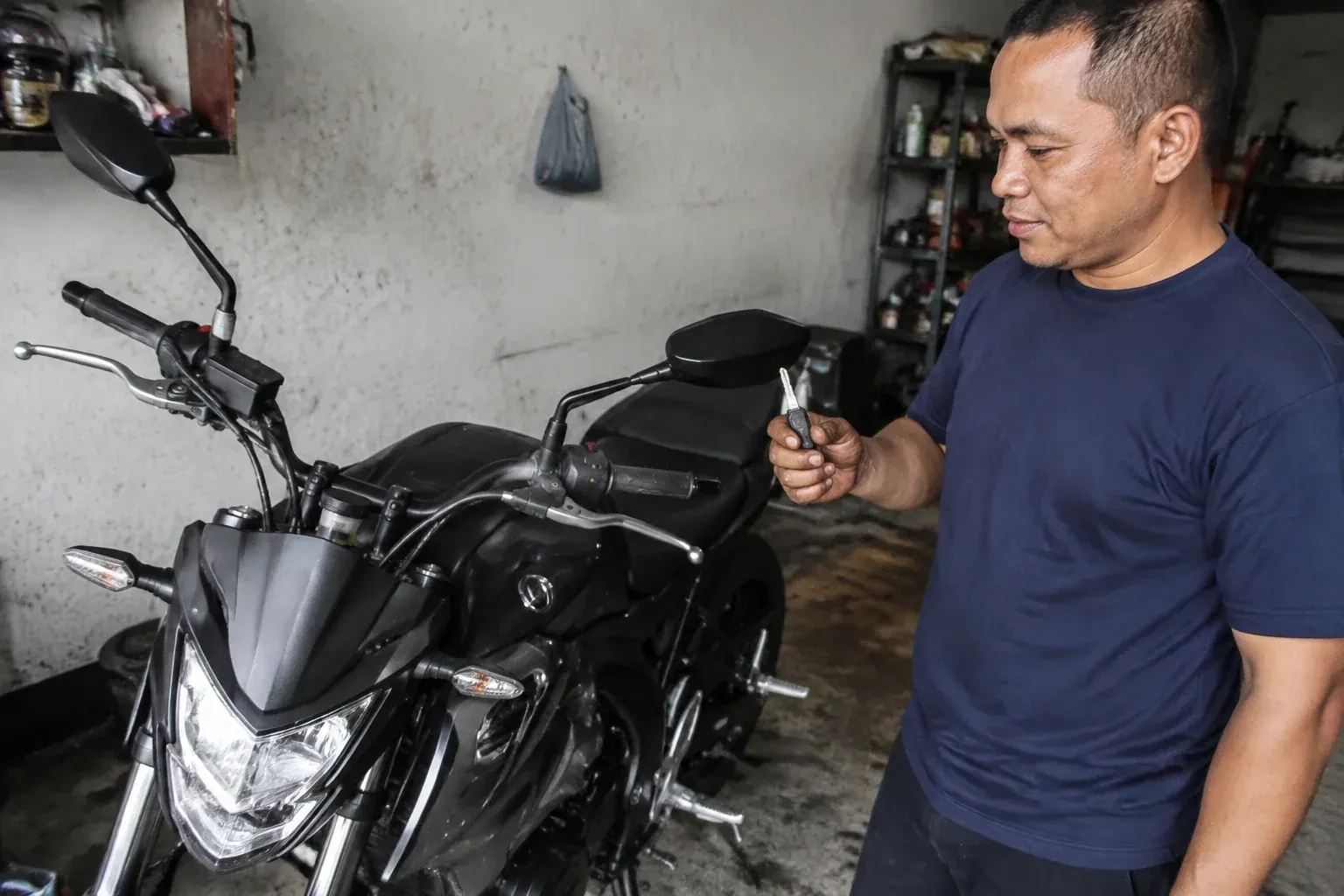 Person holding a key beside a black motorcycle in a garage. — Motorcycle & Scooter Keys, Oakville