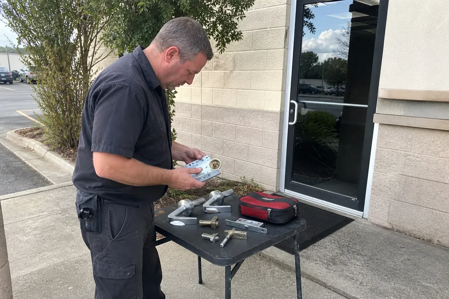 Technician examining detached commercial lock hardware on a table outside a shop entrance. — Business Lockout Service, Oakville