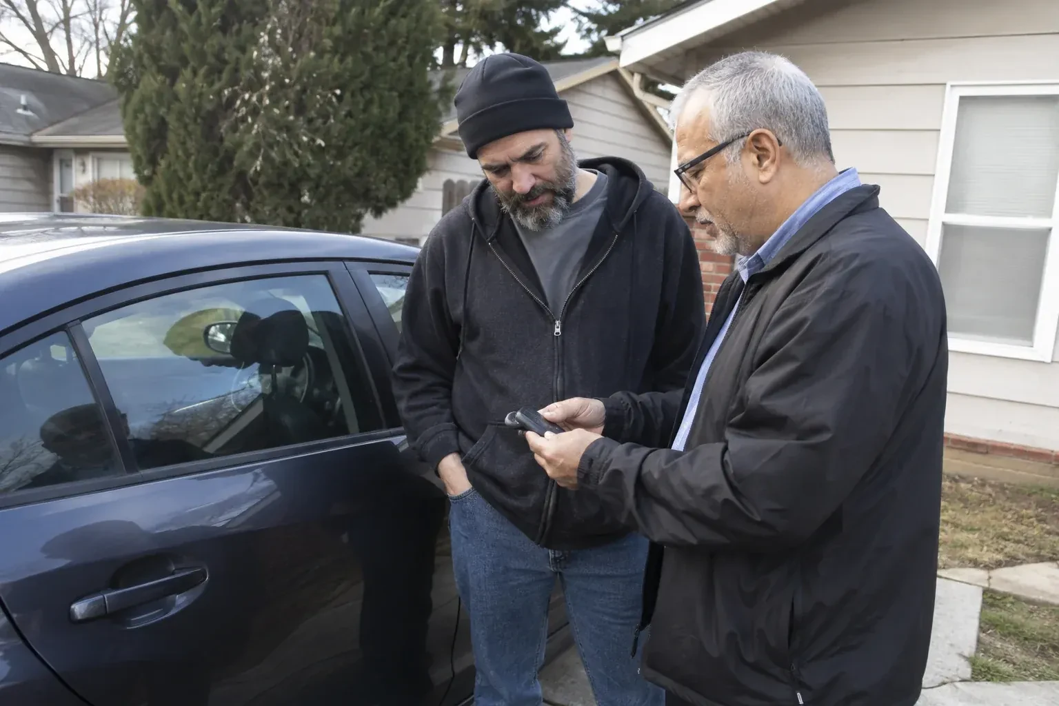Two adults discussing a key fob beside a parked car. — Car Lockout Service, Oakville